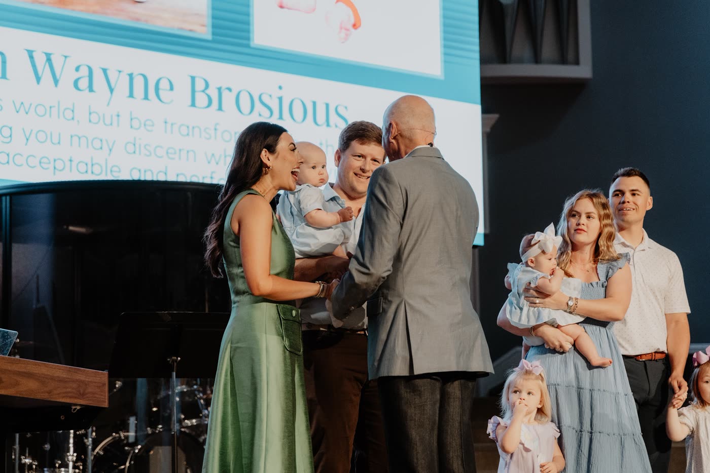 David McKinley praying with a young family holding their baby at a parent commissioning